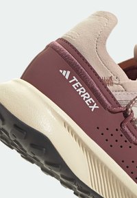 Gros plan du talon de la chaussure Terrex bordeaux et beige avec une semelle noire texturée et un col rembourré.