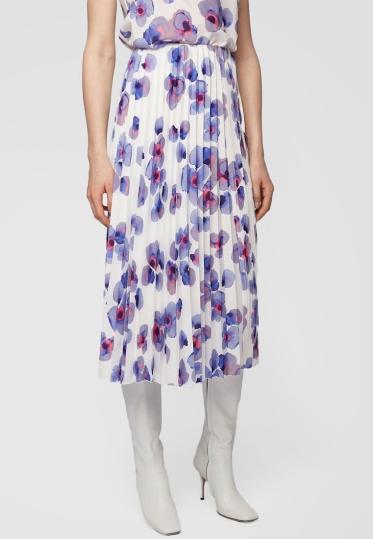 Femme portant une jupe midi plissée blanche avec un motif floral violet et rose, associée à des bottes blanches hautes à talons.