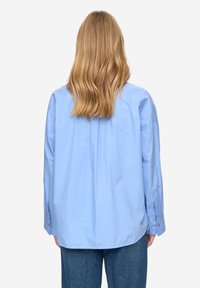 Camicia azzurro chiaro a maniche lunghe con vestibilità ampia, caratterizzata da un giogo posteriore e polsini con bottoni, realizzata in tessuto di cotone liscio.