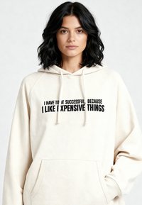 Felpa con cappuccio color crema realizzata in tessuto morbido, con tasca frontale e cappuccio con coulisse. Testo nero sul davanti: "DEVO AVERE SUCCESSO..."