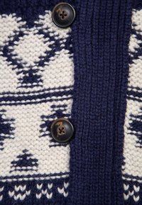 Marinblå och krämfärgad stickad kofta med geometriskt mönster, texturerad tyg och två svarta knappar framtill.