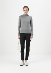 Grå langærmet turtleneck skjorte, sorte tætsiddende bukser, hvid struktureret håndtaske og hvide slip-on sko, sat mod en hvid baggrund.