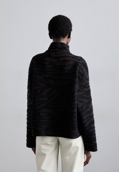 Jersey negro de gran tamaño con cuello alto, patrón de cebra texturizado, tejido suave y hombros caídos, combinado con pantalones color crema.