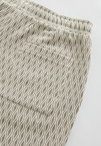 Geweven beige broek met een textuur van wit diamantenpatroon. Voorzien van een elastische taille en een zijzak aan de achterkant.