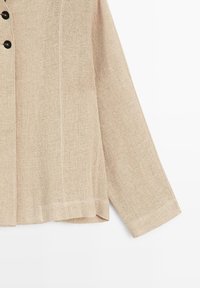 Beige langærmet jakke med linnedstruktur og sorte knapper foran, præsenteret på hvid baggrund.