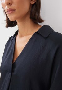 Marineblaue Bluse mit V-Ausschnitt, Kragen und weichem, strukturiertem Stoff. Sie hat einen lockeren Schnitt mit subtilen Drapierungen am Ausschnitt.