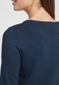 Marineblå strikket genser med rund hals og subtile sømdetaljer bak. Myk tekstur og tettsittende design.