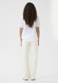 T-shirt bianco in cotone e pantaloni ampi color crema. La maglietta ha maniche corte, mentre i pantaloni presentano due tasche posteriori e una vestibilità comoda.