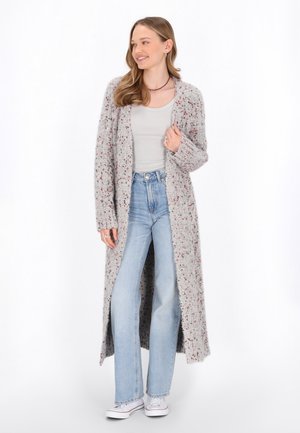 Cardigan lungo grigio con un motivo a maglia testurizzata, caratterizzato da spruzzi di colori multipli. Con apertura frontale, polsini a costine e spacchi laterali. Indossato sopra una camicia chiara e jeans blu.