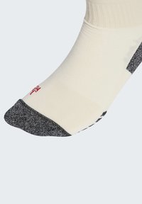 Bílá ponožka se šedou špičkou a patou, červeným označením "L" blízko špičky a černými vzorovanými protiskluzovými body na podrážce.