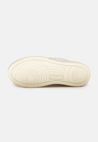 Semelle de sneaker de couleur claire avec une surface lisse et texturée. Présente des motifs circulaires et un logo discret près du talon.
