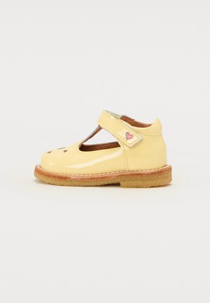 Gul patentlæder Mary Jane sko med udskæringer, Velcro strop og lyserøde hjerteaccenter. Flad gummisål med syet detalje.