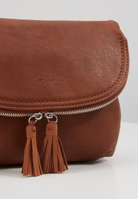 Borsa in pelle marrone con chiusura a patta, dotata di zip argentata e due nappine marroni. Superficie testurizzata e dettaglio di cucitura sottile.