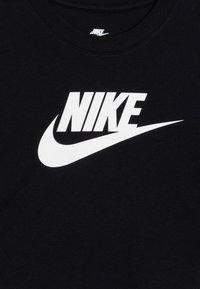 Melna kokvilnas t-krekls ar lielu balto Nike logo pāri priekšai. Kakla vietai ir ribota tekstūra.
