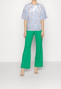 Blusa de estampado floral azul claro con mangas abullonadas, combinada con pantalones de pierna ancha verdes y texturizados, y sandalias beige.