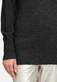 Pull en maille noir avec un ourlet côtelé, doté d'une surface texturée et de légers brillants métalliques. Associé à un pantalon argenté brillant.