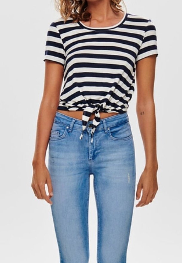 Pruhovaný krátký rukávový crop top v námořnické modré a bílé barvě, s detailem uzlu vpředu. Spárováno s světle modrými obepnutými džíny.