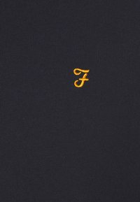 Suéter de punto azul marino con un pequeño logotipo bordado en amarillo con la letra "F". El material es suave, con una textura fina y un acabado de costura uniforme.