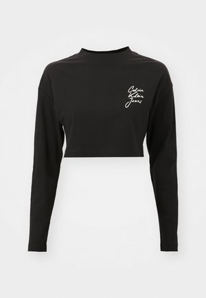 Svart langermet crop topp laget av myk bomull, med høy krage og en hvit logo på venstre brystområde.