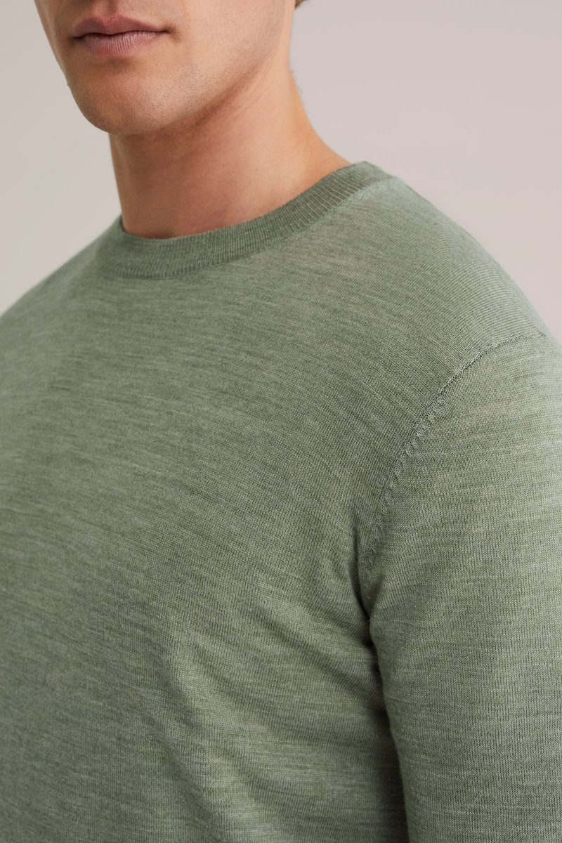 Ljusgrön stickad tröja med rund halsringning och korta ärmar. Texturen är slät med ett subtilt melerat mönster.