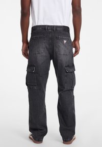 Pantaloni cargo din denim negru, cu multiple buzunare pe lateral, design drept și logo brodat pe spate. Material texturat cu un finisaj ușor decolorat.