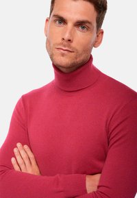 Pull à col roulé ajusté en rose vif, fabriqué en tissu côtelé, avec un col haut et des manches longues à la texture lisse.