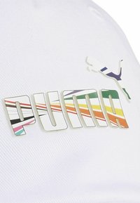 Șapcă albă cu un logo „PUMA” proeminent, format din dungi colorate îndrăznețe, și un mic logo siluetă deasupra, pe un material texturat.