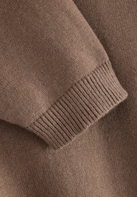 Détail d'un pull en tricot marron avec une texture côtelée aux poignets. Tissu doux et léger avec une finition lisse et une légère variation de couleur.