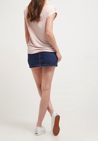 Top de color rosa claro, de manga corta, con un patrón de puntos, combinado con una falda mini de mezclilla oscura y zapatillas blancas con suelas texturizadas.