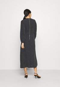 Černé midi šaty s puntíky a dlouhými rukávy, mají zip vzadu a volný střih. Nosené s černými podpatky.