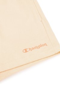 Fioletowe szorty bawełniane w kolorze brzoskwiniowym z małym logo "Champion" w ciemniejszym odcieniu w pobliżu dolnego brzegu. Miękka tekstura i prosty design.