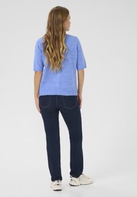 Light blue knitted sweater with short sleeves, paired with dark blue jeans and white sneakers. Long wavy hair falls down the back.