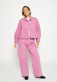 Rozā kordurojas jaka ar strukturētu apkakli un plecu detaļām, saskaņota ar plāna stila biksēm. Gluda tekstūra, ikdienišķs dizains.