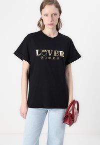 Juoda medvilninė marškinėliai su aukso metalo "LOVER PINKO" užrašu, laisvas siluetas, trumpomis rankovėmis, derinami su šviesiai mėlynomis džinsais ir raudona pinigine.