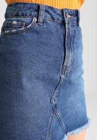 Denim rok met een rafelige zoom, lichtblauwe kleur, verweerde details en een klassiek ontwerp met vijf zakken en metalen accenten.