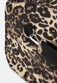 Saco de estampado de leopardo com um tecido texturizado em bege e preto, com um fecho de metal prateado e uma alça preta resistente. Forma arredondada.