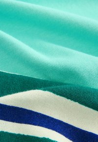 Neulottu kangas turkoosin, vihreän, valkoisen ja sinisen sävyissä, jossa on teksturoituja raitoja. Pehmeä pinta, jossa näkyvät ompeleet ja lievä kiilto.