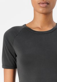 Short-sleeved, dark gray top made of smooth fabric with a crew neckline and subtle stitching details.