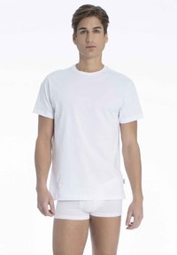Hvid bomulds-T-shirt med korte ærmer, rund hals og en afslappet pasform. Båret sammen med hvide boxershorts, mod en ensfarvet baggrund.