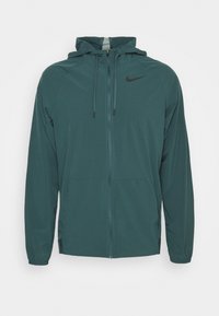 Chaqueta Nike de color verde oscuro con cierre de cremallera, capucha y cordones ajustables; cuenta con un bolsillo delantero y un sutil acento de logo.