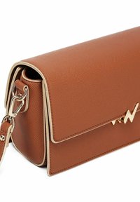 Hnědá kožená crossbody taška s texturovaným povrchem, zlatým kováním a kontrastním krémovým lemováním, obsahující klopový uzávěr a dekorativní detaily.