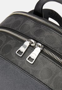 Mochila de couro preta texturizada com fechos de correr prateados duplos, costura em contraste e uma alça superior para facilitar o transporte.