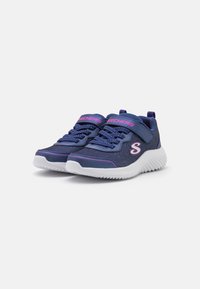 Une paire de baskets pour enfants bleu marine avec des semelles blanches, des accents roses, des lacets et une sangle à scratch sur fond blanc.