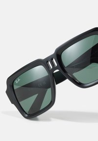 Ochelari de soare dreptunghiulari negri cu lentile verzi, având un design de cadru îndrăzneț și accente decupate în partea superioară, marcați cu brandul Ray-Ban.