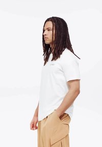 White short-sleeve t-shirt with round neckline. Worn with beige cargo pants featuring pockets and logo embroidery on the leg.