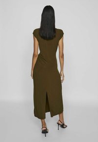 Olivovo zelené šaty po kolená s krátkymi rukávmi, textúrovaná látka a rozparok vzadu. Nosené s čiernymi sandálmi na vysokých podpätkoch.