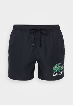 Shorts de baie negri, dintr-un material ușor, cu talie elastică și șnur de ajustare. Un logo cu un crocodil verde și textul "LACOSTE" sunt imprimate pe lateral.
