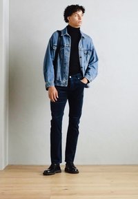 Denimska jakna, črn turtleneck, temni kavbojke in črne čevlje. Priložnostna obleka z udobnim krojem in minimalnim stilom, stoji na lesenih tleh.