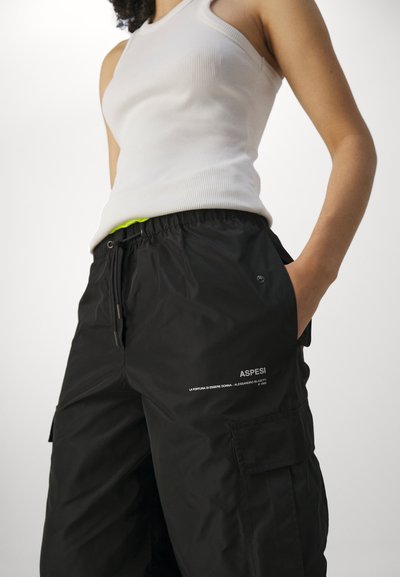 Zwarte cargobroek met elastische tailleband, zijzakken en witte logo-detail. Gecombineerd met een aansluitend wit geribd tanktop.