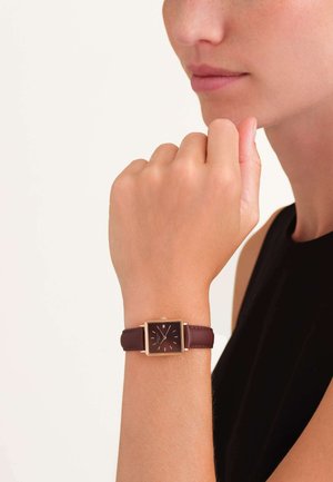 Montre carrée avec un cadran marron foncé, des accents dorés et un bracelet en cuir bordeaux. Marqueurs d'heure simples et design minimaliste.